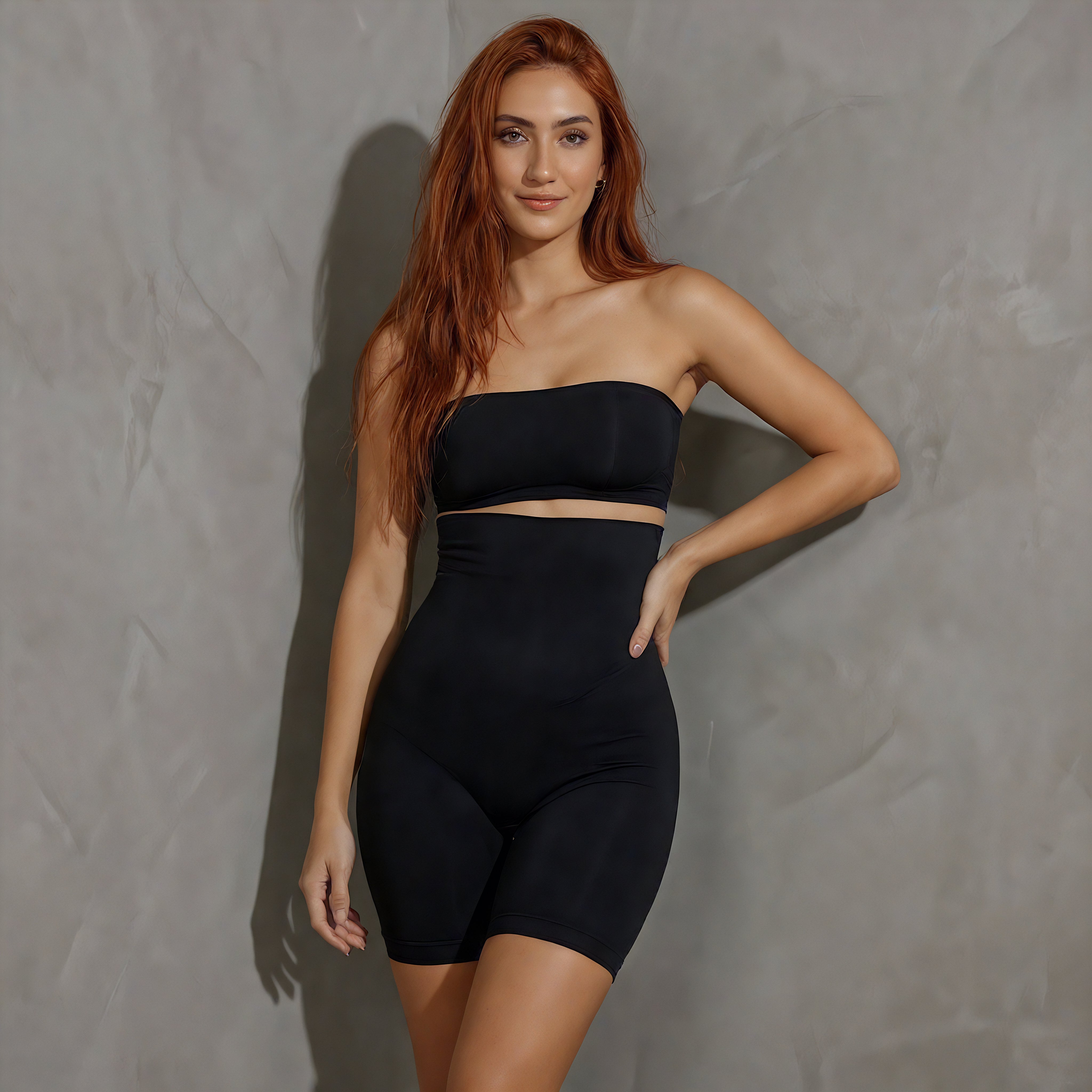 Woman wearing a black strapless top and high-waisted shorts against a gray background also wearing black shapewear from lyvia