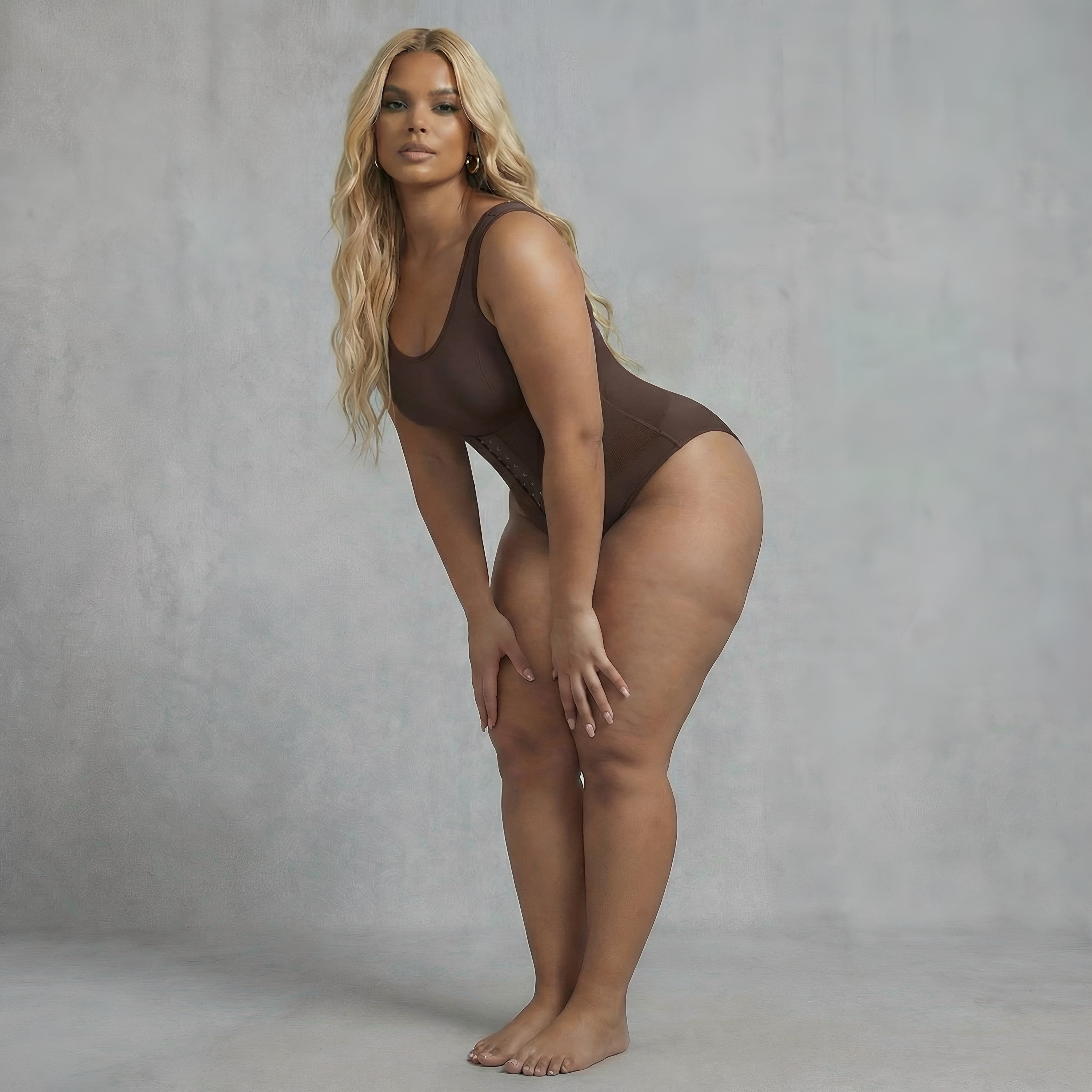 Woman wearing a brown bodysuit against a gray background. Curvy womans shapewear bodysuit brown lyvia shapewear.