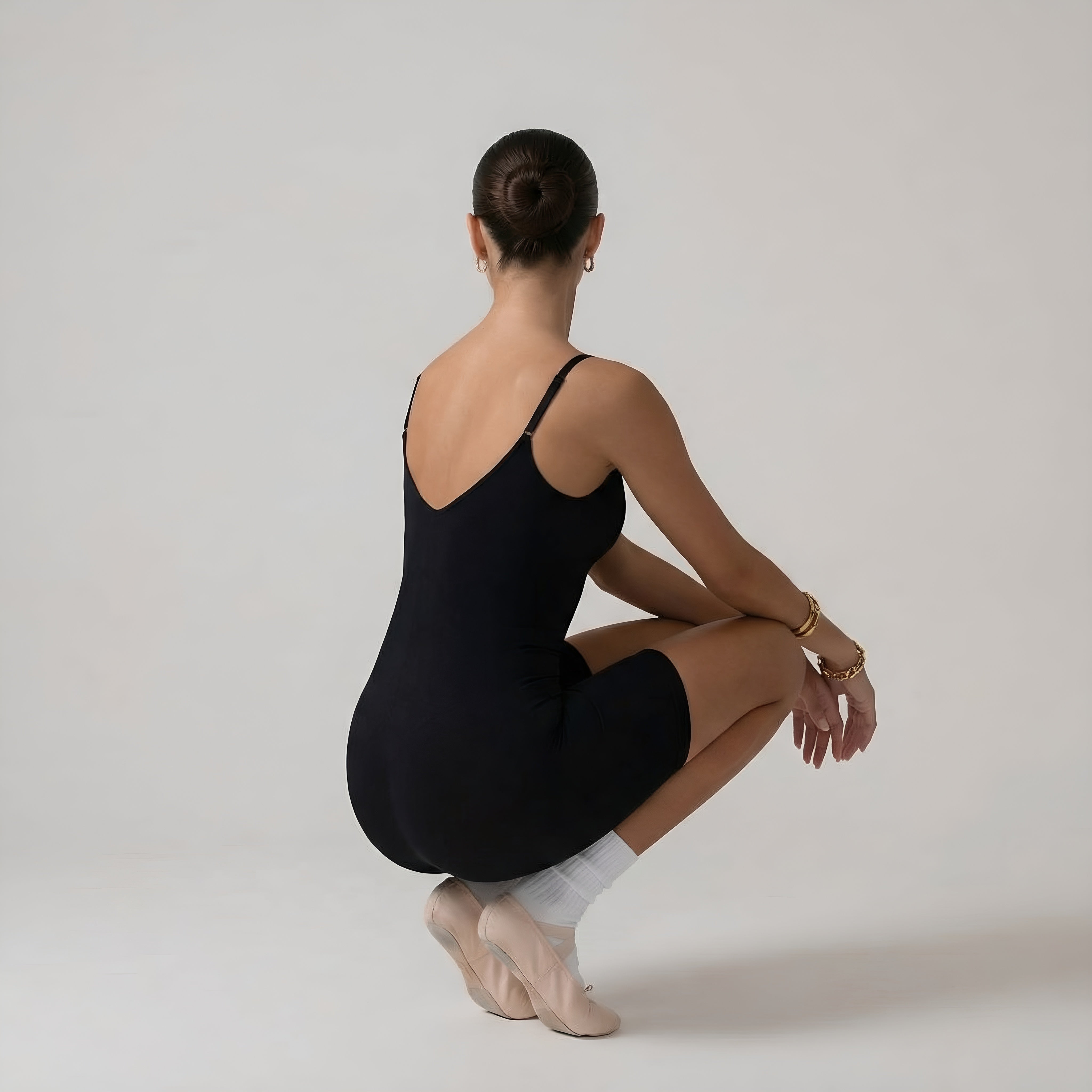 Person wearing a black leotard sitting on a white floor with a neutral background. Black shapewear womans jumpsuit lyvia.