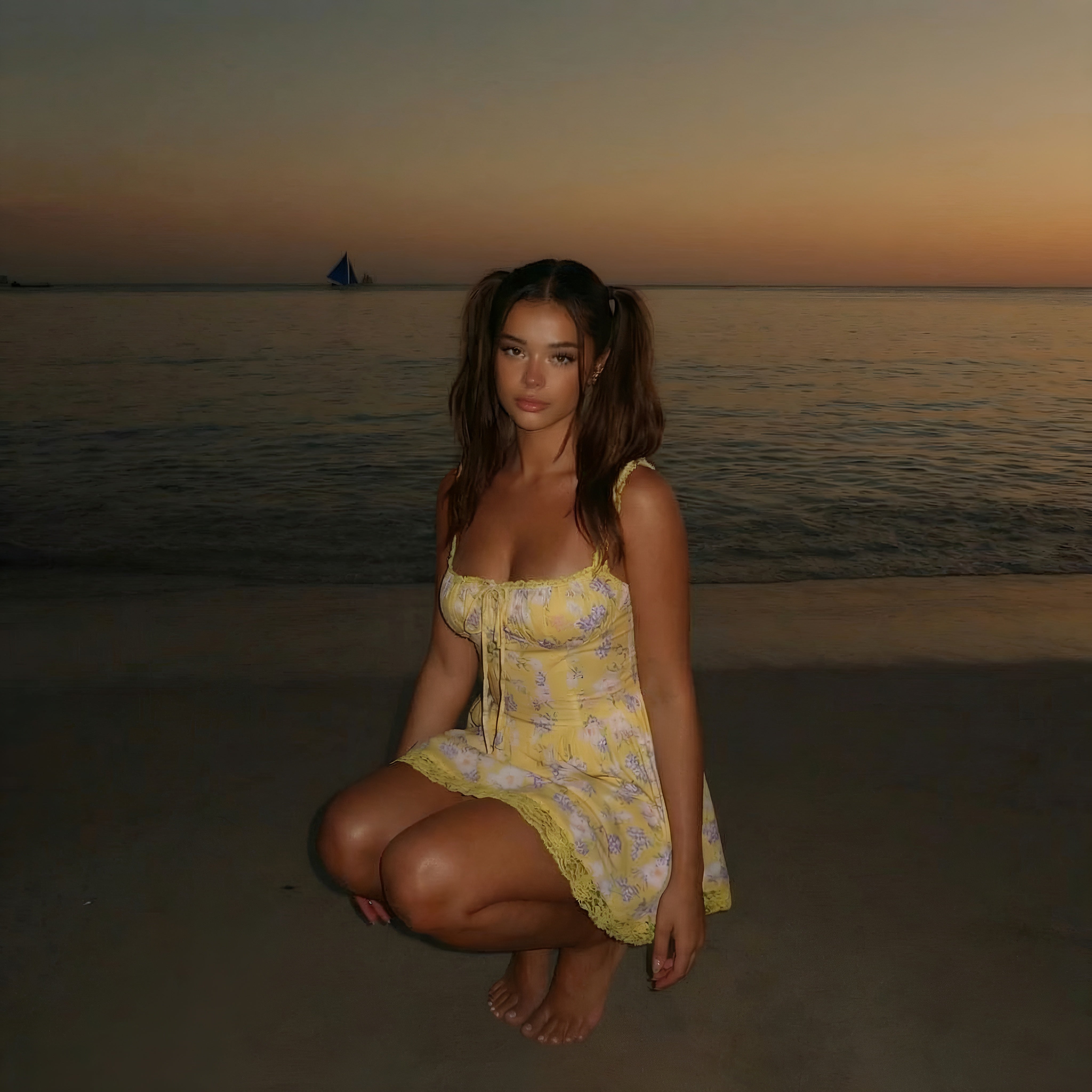 Woman in a yellow dress squatting on a beach at sunset. LYVIA Yellow Floral Meadow Bloom Mini Dress.